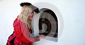 Blond woman in red historic costume old fashioned looking in the secret window