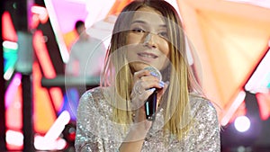 Blond woman singer with microphone on stage with spotlights, interactive screen