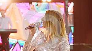 Blond woman singer with microphone on stage with spotlights, interactive screen