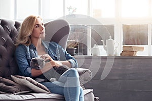 Blond woman sitting with cat on couch.