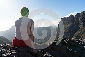 Blond woman sitting with contemplation, enjoying the moment on the sunset in the mountain, relaxing and dreaming. Adolescent girl