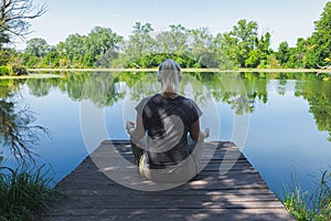 Blond woman sitting in yoga pose on wooden pier on the lake