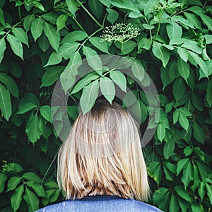 Blond woman standing backwards beside the trees.