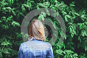 Blond woman standing backwards beside the trees.