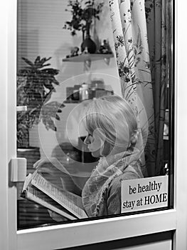 Blond woman stay home and reads book near window. Self isolating while quarantine concept. Education and rest at home