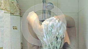 Blond woman touching her hair, water falling down from shower head in bathroom and wet her hair with water, body care concept