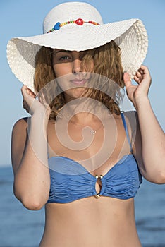 Blond woman wear blue bikini and white hat standing at the sea