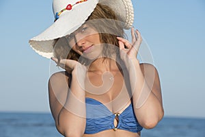 Blond woman wear blue bikini and white hat standing at the sea