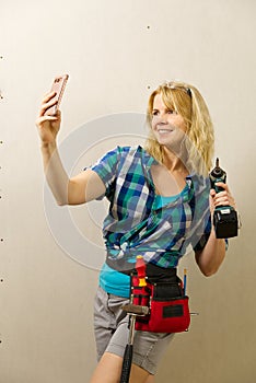 Blond woman wearing a DIY tool belt full of a variety of tools on a unpainted plasterboard wall background. Construction woman