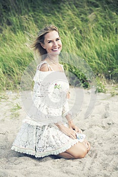 Blond woman in white dress sitting on the beach
