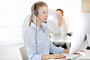 Blond woman working in sunny call center. Group of diverse people working as customer service occupation. Business
