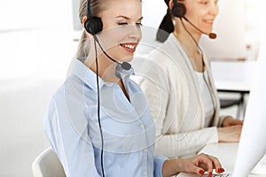 Blond woman working in sunny call center. Group of diverse people working as customer service occupation. Business