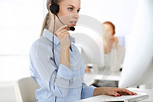 Blond woman working in sunny call center. Group of diverse people working as customer service occupation. Business