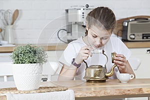 Blond young girl looking inside of empty copper teapot for coffee, sitting at table in kitchen