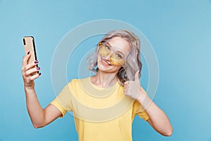 Blond young happy woman in the tellow t-shurt and sunglasses in the blue studio.