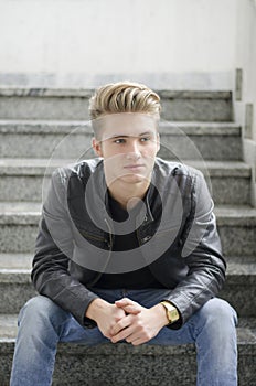 Blond young man sitting on stairs outside