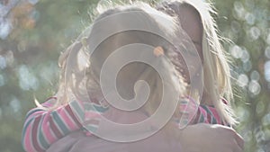 Blond young woman hugging and kissing her daughter in sun light close up. Happy family. Mother and her child resting in