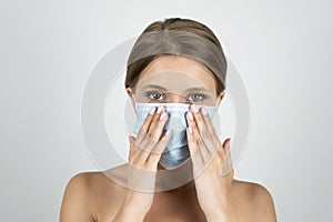 Blond young woman wearing medical mask holding hands near her face close up isolated white background