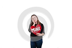 Blond youthful female holding red heart shaped sign word MINE painted on sign on solid white background