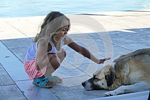 Blonde 4 year old girl caresses a dog