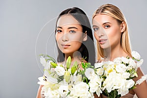 Blonde and asian brunette naked women with flowers isolated on grey