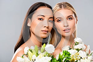 Blonde and asian brunette naked women with white flowers  on grey