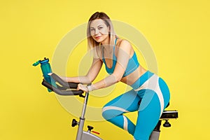 Blonde athletic woman on exercise bike with bottle of water in hands, fitness and diet concept.