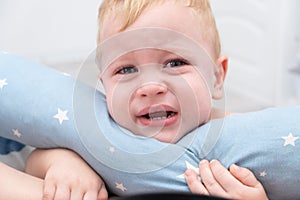 Blonde baby boy crying hugging a pillow.