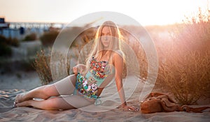 blonde in a bathing suit lying on the sand at sunset