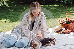 Blonde beautiful girl sitting on white blanket in garden and having picnic at sunny day with cute puppies.