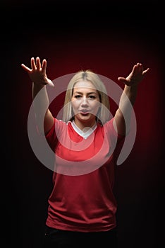 Blonde beautiful woman football fan chanting with both arms raised in red T shirt