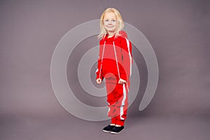 Blonde blue-eyed little model girl in a red sports suit posing in the studio on a black background.active childhood full