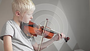 A blonde boy learns to play the violin at home