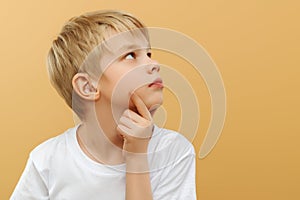 Blonde boy . Let me think . Thoughtful clever schooler in white shirt with puzzled serious expression , child