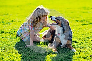 Blonde boy playing with dog on the lawn in the park. His pet attentively looks at the owner. Child with pet puppy dog