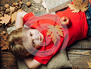 Blonde boy resting with an apple on stomach lies on wooden floor in autumn leaves. The biggest discounts for all autumn