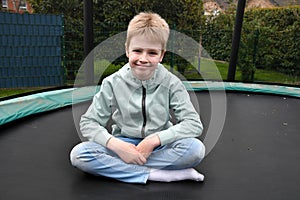Blonde boy sitting in tailor\'s seat on his trampoline