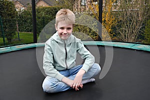 Blonde boy sitting in tailor\'s seat on his trampoline