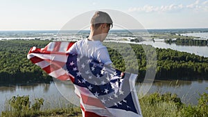 Blonde boy waving national USA flag outdoors over blue sky at the river bank