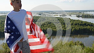 Blonde boy waving national USA flag outdoors over blue sky at the river bank