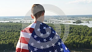 Blonde boy waving national USA flag outdoors over blue sky at the river bank