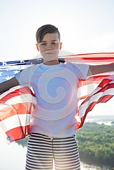 Blonde boy waving national USA flag outdoors over blue sky at the river bank