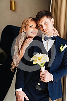 the blonde bride gently hugs the groom's shoulders by the window.