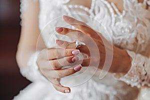 Blonde bride in long sleeve lace dress standing in her room, posing and putting on her engagement ring.