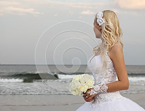 Blonde bride walking on the the beach. beautiful woman in wedding dress looking on the ocean.