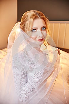 Blonde bride in a white wedding dress and a long veil is waiting