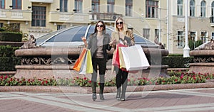 Blonde and brunette fashion women meet each other in the city center after shopping.