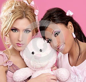 Blonde and brunette girls hug a pink teddy bear