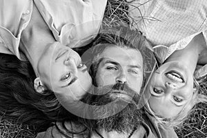 Blonde and brunette lay on his shoulders. Man fall in love both women. Happy threesome. Man bearded hipster lay on grass