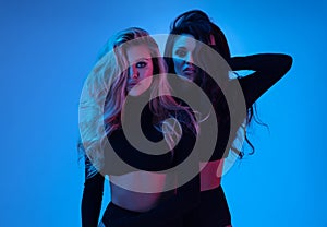 Blonde and brunette models in black clothes looking at camera and posing in studio